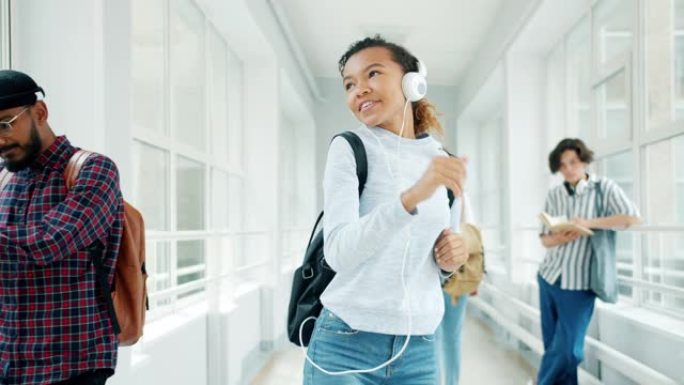 开朗的女学生在学校大厅里戴着耳机跳舞，欣赏歌曲