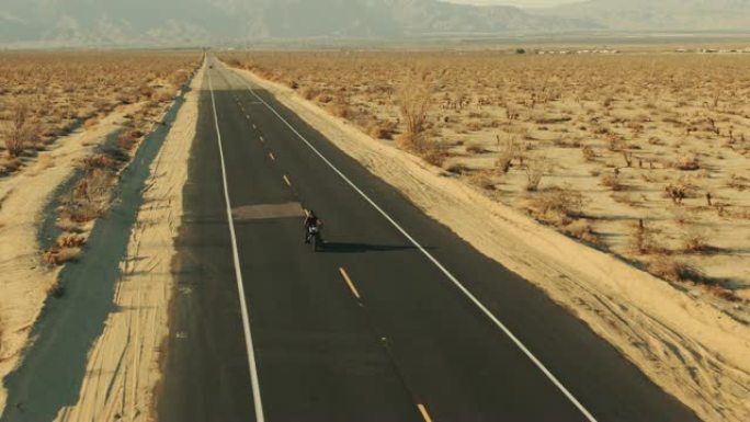 日落时在沙漠路上骑摩托车的人的鸟瞰图