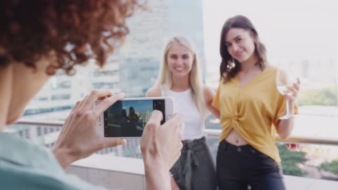 年轻女子与女友在城市阳台上喝酒的智能手机拍照，特写