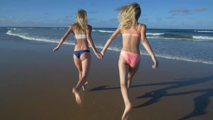 南非海滩上两个美丽的年轻女子在海浪中奔跑的4k后视图