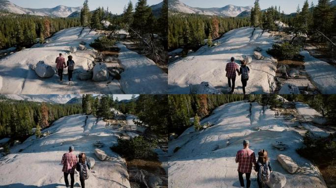 无人机摄像机跟随年轻浪漫的情侣一起沿着约塞米蒂国家公园森林的惊人白岩徒步旅行。
