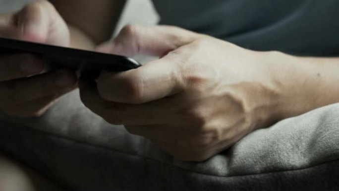 亚洲男子坐在沙发上，在家中智能手机上玩在线流媒体社交媒体游戏。技术概念