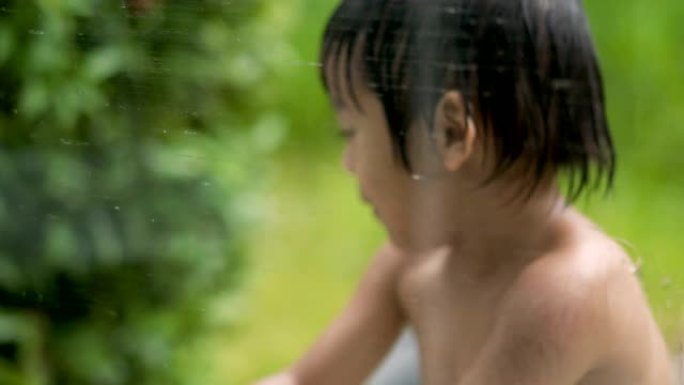 4k实时顽皮的男孩在花园里的湿玻璃后面玩耍