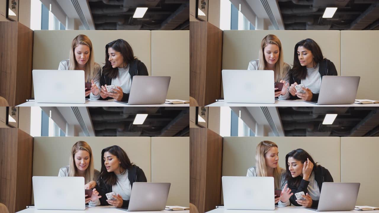 两名年轻的女商人在现代开放式工作空间中并肩工作，检查手机