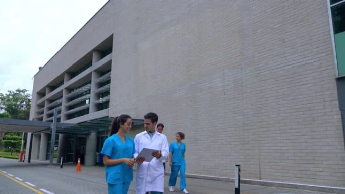 开朗的医护人员走出医院，一边谈论一个看着平板电脑的病例
