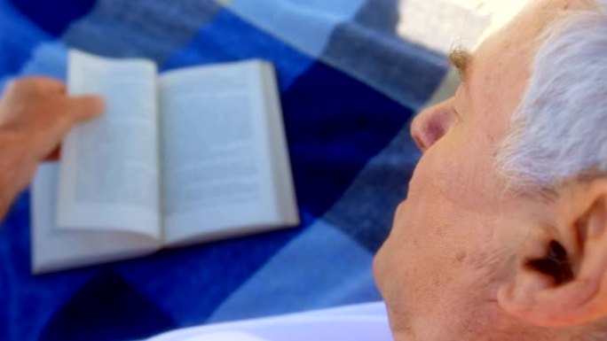 活跃的高加索高级男子在海滩上读书的特写4k