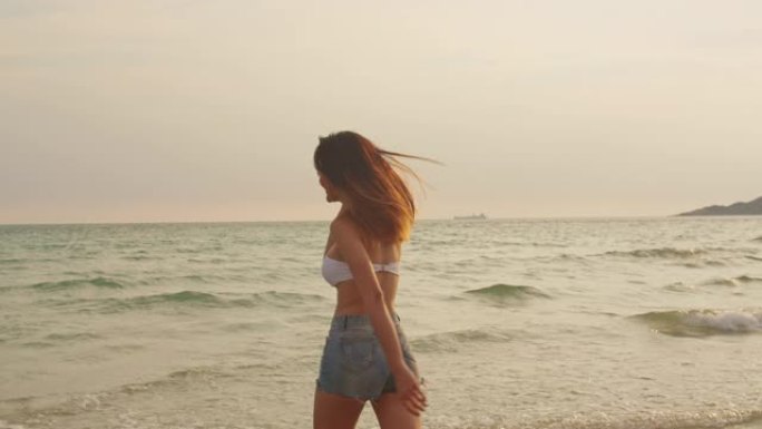 在沙滩上跑步的亚洲女人。年轻快乐的女性在比基尼放松和有趣的热带海时，日落而度假，夏季旅行的概念。慢动