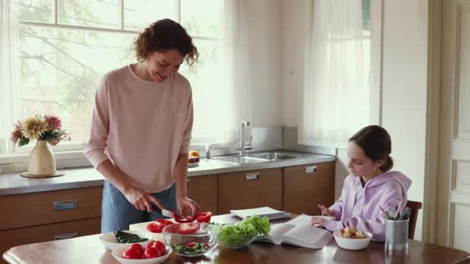 妈妈准备蔬菜沙拉，而十几岁的女儿在厨房学习