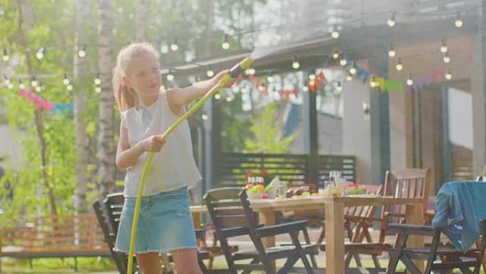 可爱的小女孩在花园里玩水管洒水器。阳光明媚的夏日孩子在后院玩耍。慢动作。