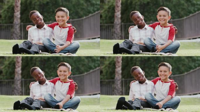 两个青春期前的男性朋友坐在草地上，双臂环抱，对着镜头微笑