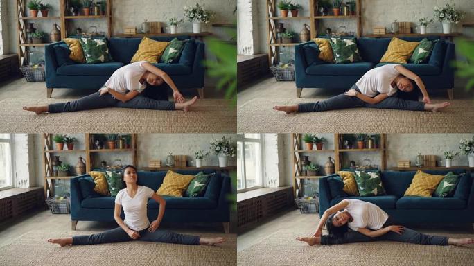 苗条的亚洲女士正在家里做运动，伸展身体、手臂和腿，坐在地板上享受活动和健康的生活方式。体育和千禧一代