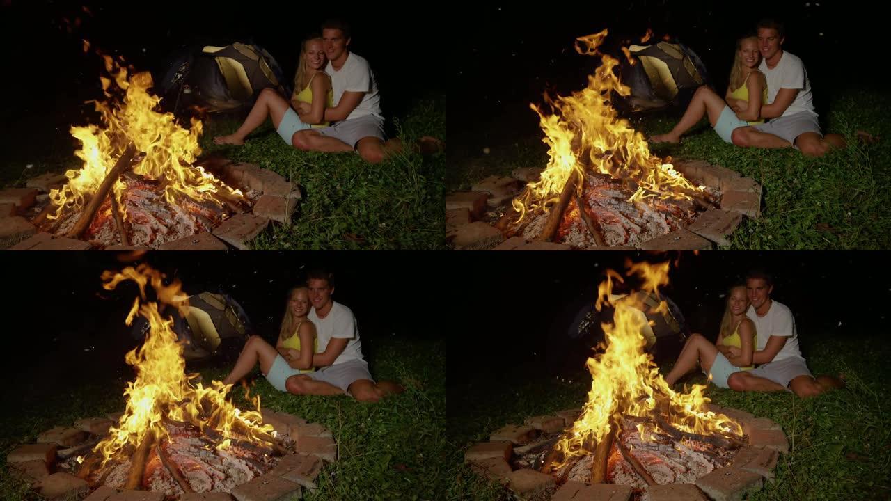 慢动作: 无忧无虑的旅游夫妇在野外露营，在火炉旁拥抱。
