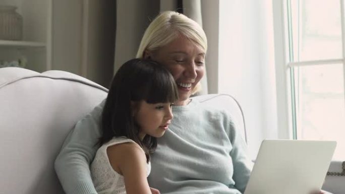 快乐成熟的奶奶和好奇的小孙女使用笔记本电脑