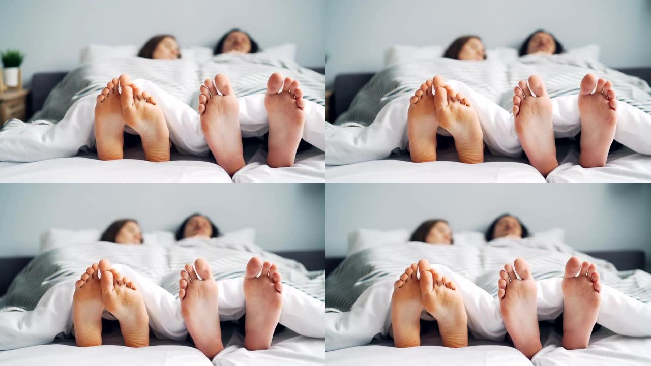 女孩和男孩夫妇赤脚躺在毯子下一起在床上打盹