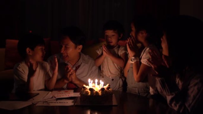 庆祝和家庭概念-快乐的父亲在家里的晚宴上在生日蛋糕上吹蜡烛。