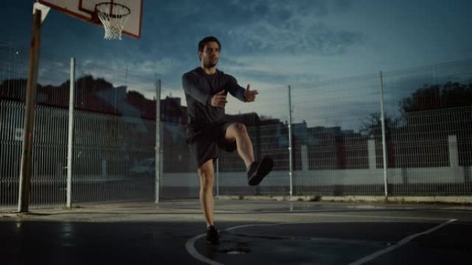 穿着运动服的强壮肌肉健康的年轻人做腿部和平衡锻炼。他正在一个有围栏的室外篮球场里锻炼身体。居民区下雨