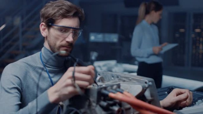 专业的汽车工程师在眼镜与计算机和检查工具正在测试使用的电动发动机在高科技实验室与概念车底盘。