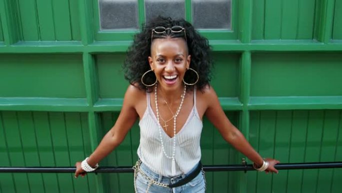 年轻的黑人妇女靠在城市街道上的绿色墙壁上的扶手上大笑，高角度