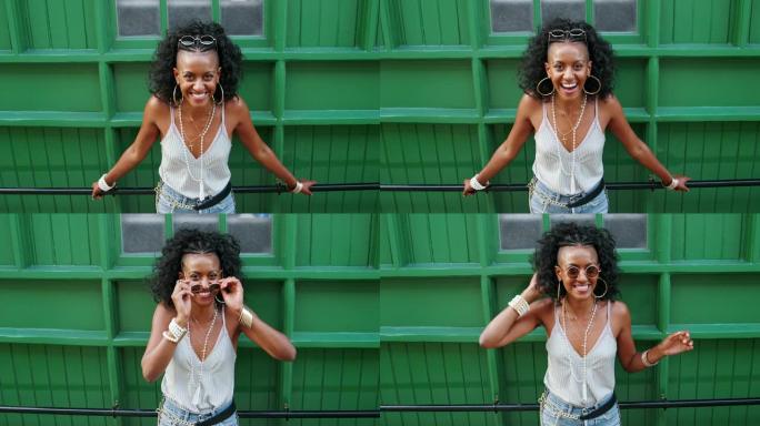 年轻的黑人妇女靠在城市街道上的绿色墙壁上的扶手上大笑，高角度