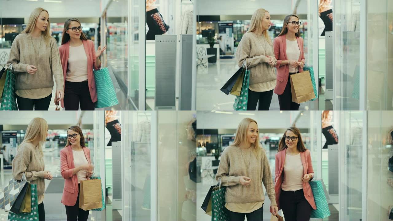 迷人的年轻女士在现代购物中心里聊天，沿着窗户走，然后看着新的内衣系列打手势并进行讨论。
