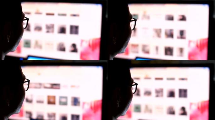 男人晚上在电脑上工作，通过眼镜看电脑屏幕