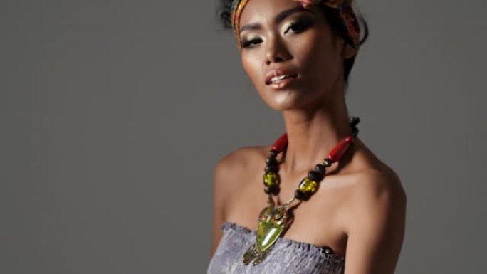 年轻漂亮的时尚模特，具有传统的非洲风格，深色背景上有围巾，耳环和化妆。黑色后台上深色皮肤模特的侧视图