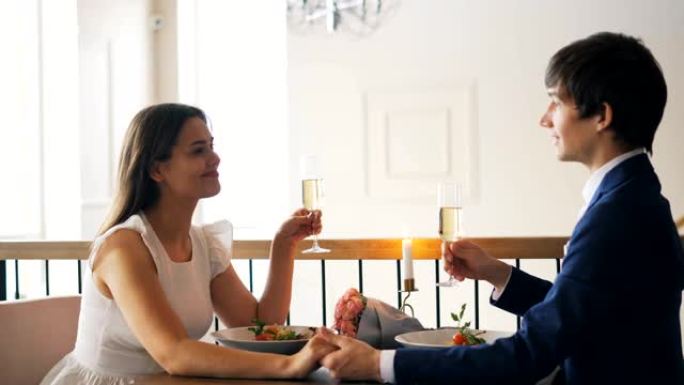 充满爱心的年轻人正在与未婚妻交谈，他们拿着香槟杯，然后在餐厅浪漫约会时碰杯并喝酒。青春和约会概念。
