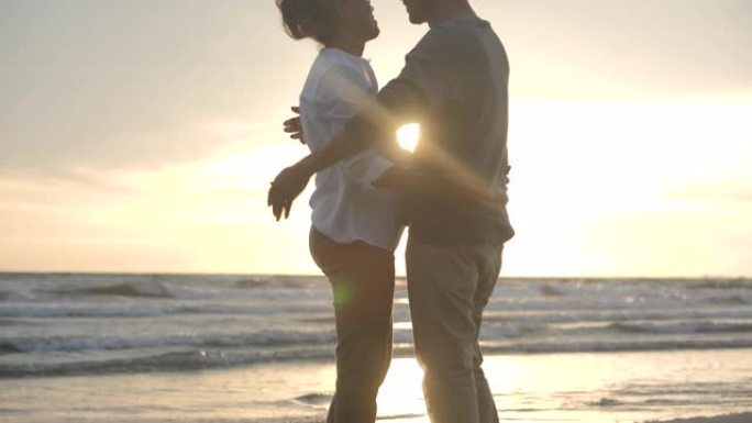 亚洲高级夫妇在日落时在海滩上慢动作拥抱。