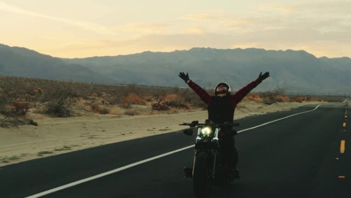快乐的人在日落时骑着摩托车在空中举起手臂庆祝