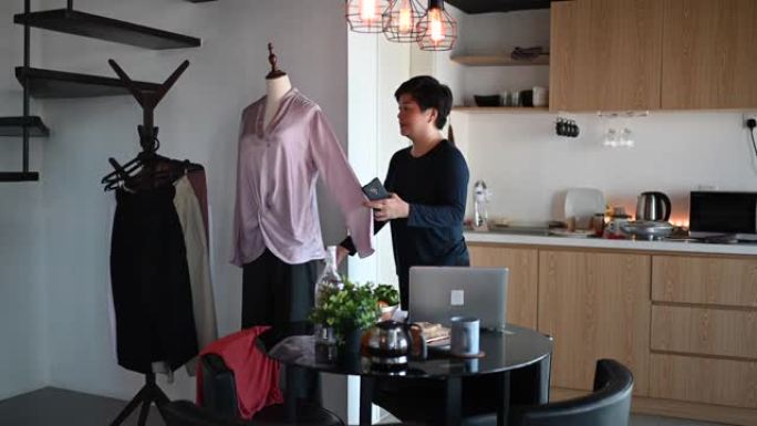 一位亚洲中国中年妇女在她的饭厅里设置人体模型并用布打扮成网上购物业务目录