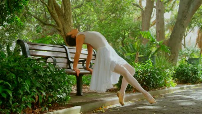 美丽的年轻芭蕾舞演员在公园4k的长凳上做伸展运动