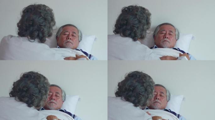 年迈的妻子正在家里的床上照顾生病的丈夫。通过用手触摸丈夫的额头来测量发热，并注意不远处的症状