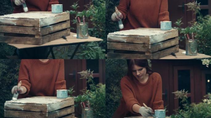 在花园里DIY。女人画木箱。
