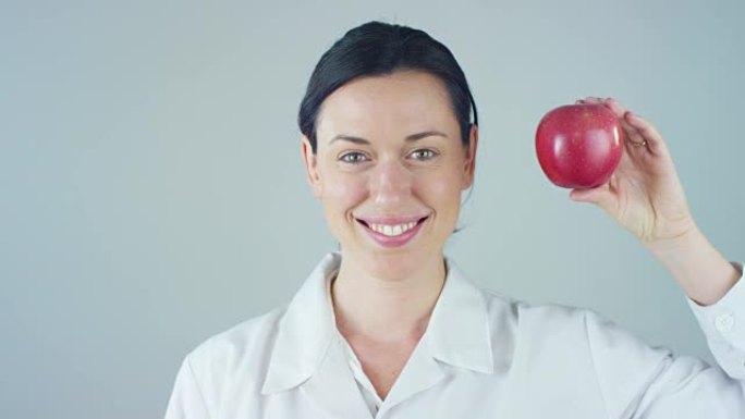 营养学家的肖像，食品和健康福利专家，微笑着看着相机，拿着一个白色背景的苹果。