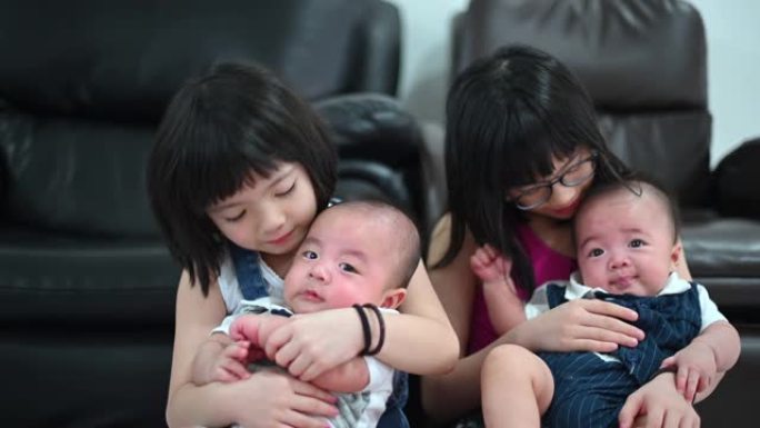 亚洲华人姐妹在客厅照顾他们的双胞胎男婴兄弟