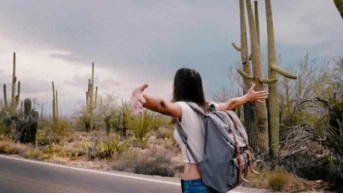 慢动作美丽的年轻快乐的旅游女人在暴风雨前张开双臂沿着沙漠国家公园路行走。