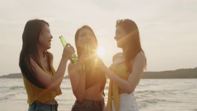 一群亚洲少女在海滩上聚会庆祝，朋友们在傍晚日落时在海上海滩上快乐地喝啤酒。户外旅游度假度假暑期概念。