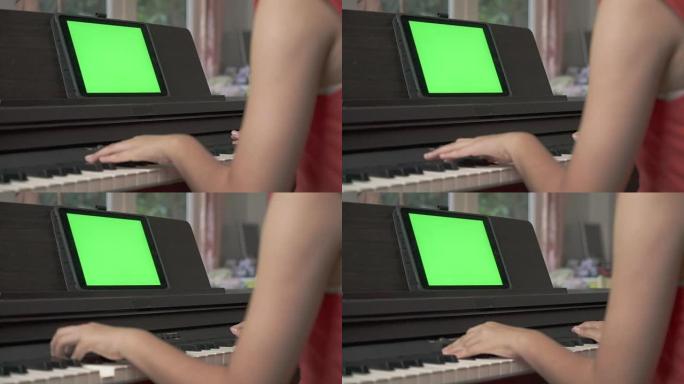 年轻的亚洲女孩在绿屏平板电脑上的钢琴在线课程上手工学习