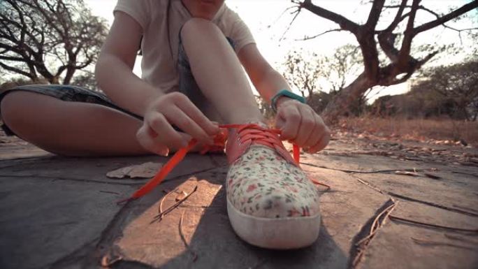 日落时分，SLO MO特写女跑步者在运动鞋上系鞋带。十几岁女孩的脚和手适合慢跑前锻炼和系鞋带。前视图