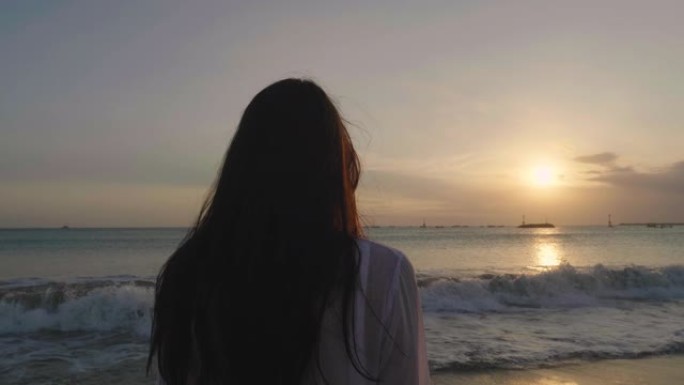 一个晒黑的女人正站在海边，看着大海，穿着白色泳衣，背景是海蓝色的水。