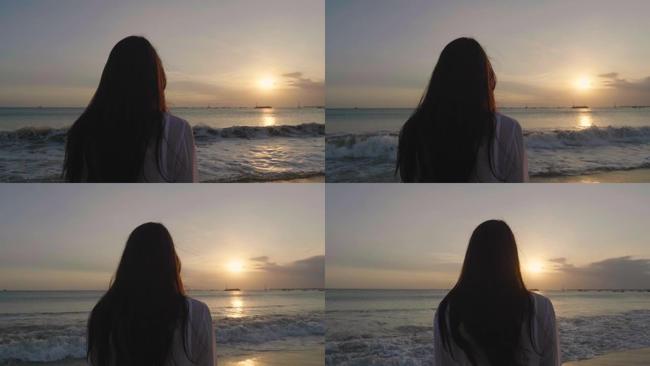 一个晒黑的女人正站在海边，看着大海，穿着白色泳衣，背景是海蓝色的水。