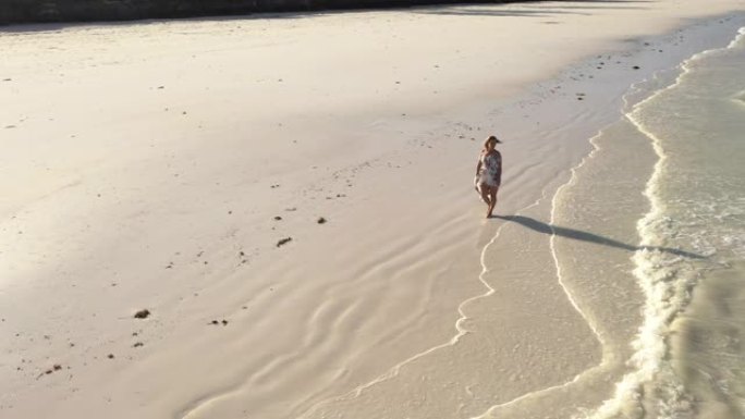 穿着太阳裙的空中女人沿着美丽的海滩散步