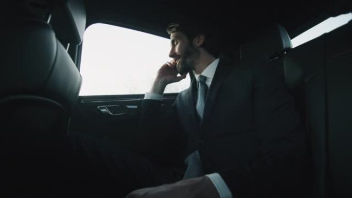 英俊的商人在一辆现代汽车旅行期间用手机打电话的慢动作与一个司机在城市中心的白天