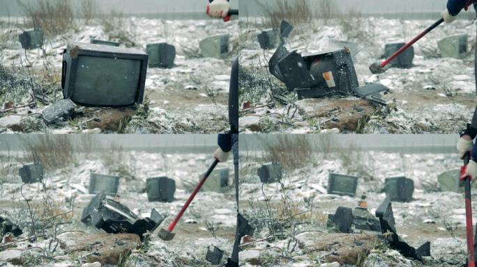 人在垃圾场用锤子打碎电视。拿着锤子的人打碎了电视屏幕。