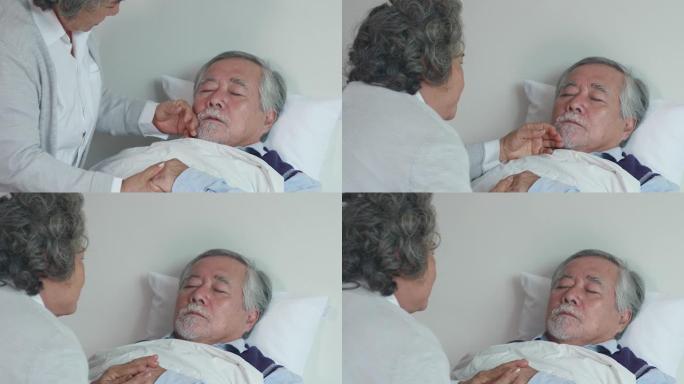 年迈的妻子正在家里的床上照顾生病的丈夫。通过用手触摸丈夫的额头来测量发热，并注意不远处的症状