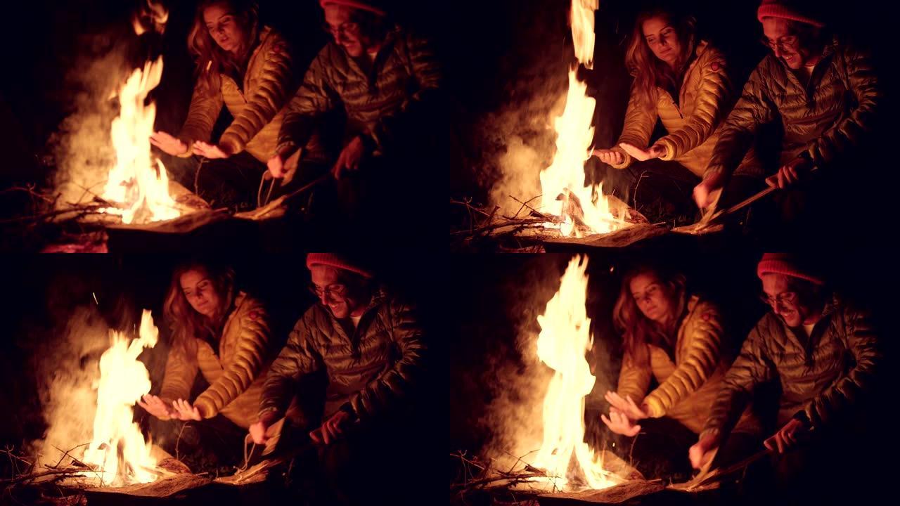 炉火边的年轻夫妇。背景中的帐篷。山地景观