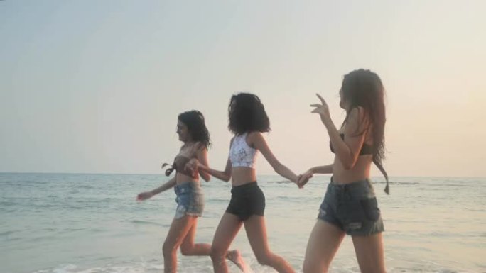 亚洲三个年轻的女性朋友在日落海滩玩得开心。海滩假期旅游概念。旅游电影