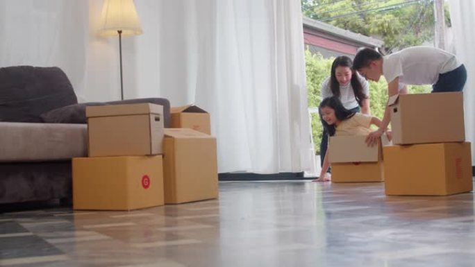 快乐的亚洲年轻家庭开心地笑着搬进新家。日本父母母亲和父亲微笑着帮助兴奋的小女孩坐在纸板箱里。新的财产