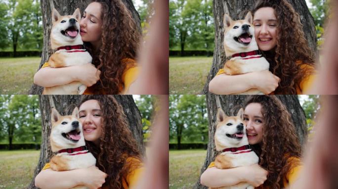 在公园里亲吻狗的女孩拿着相机自拍的特写肖像