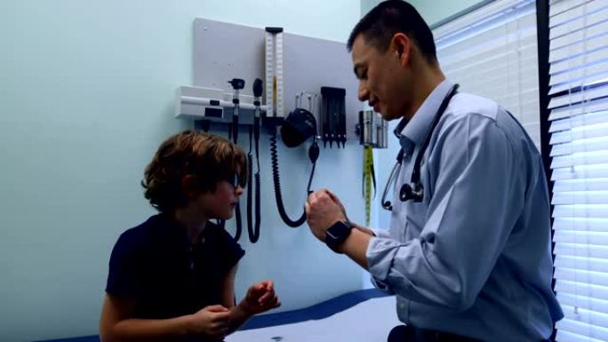 年轻的亚洲男性医生在诊所4k对高加索男孩患者手臂使用创可贴的侧视图
